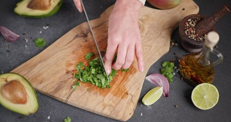 Wall Mural - Woman cutting and chopping cilantro or parsley greens on a wooden cutting board at domestic kitchen