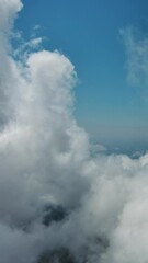 Wall Mural - Flying through beautiful white fluffy clouds in sky over blue sea. Airplane travel background. Vertical video