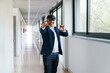 © Koldo_Studio - A businessman in a suit uses a VR headset and gestures with his hands, interacting with virtual reality in an office hallway.