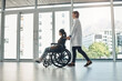 © peopleimages.com - Wheelchair, doctor and walking with patient with disability in hospital for mobility impairment, empathy and support for healthcare. Medical worker, girl and happy for leaving clinic and recovery.