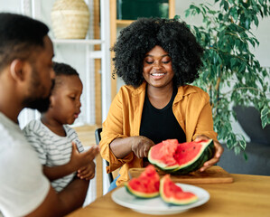 Wall Mural - child family kitchen food boy son father mother watermelon fruit slice summer organic meal fun preparing healthy diet eating home black