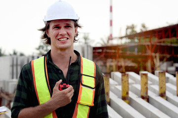 Worker engineer man with safety vest and helmet using radio walkie talkie while inspecting working area at construction building site. Young architect works at building site workplace.