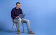 © Moon Safari - Happy male freelancer working on project over laptop while sitting on chair against blue background