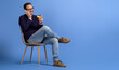 © Moon Safari - Happy young businessman sharing credit card details over phone call on chair against blue background
