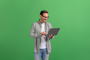 Wall Mural - portrait of happy handsome entrepreneur checking e-mails online over laptop against green background