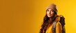 © vxnaghiyev - A young girl tourist wearing autumn clothes and carrying a camera and backpack stands against a yellow isolated background conveying a travel concept. with copy space image
