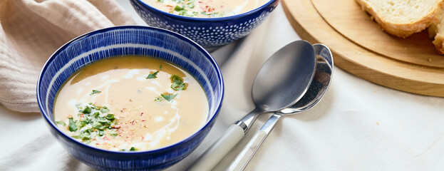 Wall Mural - Two bowls of creamy potato soup, spoons, napkin and wooden cutting board with a loaf of bread and cut pieces.