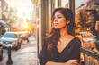 © VisualProduction - A Latina retail store manager stands proudly in front of her shop window, watching the sun set over the bustling city street.