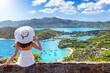 © moofushi - A tourist woman in a white dress enjoys the panoramic view over the landscape of Antigua island with English Harbour and Shirley heights