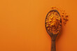 © Alexandra - Overhead view of ground turmeric spilling from a wooden spoon on an orange backdrop, showcasing the spice's rich color and texture