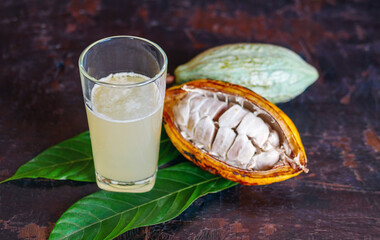 Wall Mural - Fresh cacao water in glass and half sliced ripe yellow cacao pod with white cocoa seed, Cacao juice in glass  on vintage wooden background