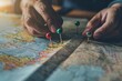 © At My Hat - A person is pointing at a map with three red pins on it. The pins are placed in different locations, indicating a journey or a planned route. The map is spread out on a table