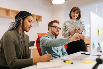 Portrait of male mentor or executive manager boss teaching diverse female internes, explaining work pointing at computer screen. Team leader supervisor training new worker instructing in modern office