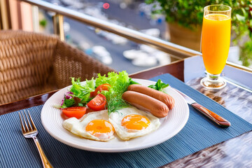 Plate of food with eggs, sausage, tomatoes, and orange juice on a table