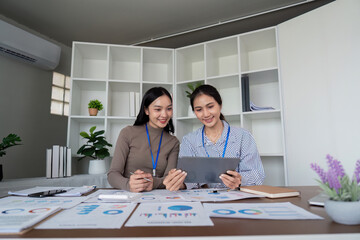Wall Mural - Two Asian women collaborating on a project in a modern office. Concept of teamwork, business, and productivity