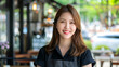 © Tanya - Asian confident smiling woman small business owner wearing uniform standing at the entrance to the cafe. Business concept.