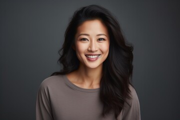 Canvas Print - Portrait of a grinning asian woman in her 30s smiling at the camera in front of soft gray background