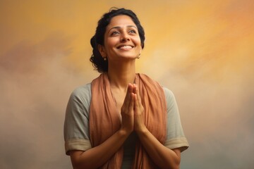 Canvas Print - Portrait of a glad indian woman in her 40s joining palms in a gesture of gratitude in pastel or soft colors background