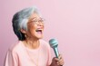 © Markus Schröder - Portrait of a smiling asian elderly woman in her 90s dancing and singing song in microphone in front of pastel or soft colors background