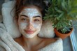 © Irina Mikhailichenko - Face peeling mask, spa beauty treatment, skincare. Happy young woman in housecoat lies relaxed with peeling mask on his face on sustainable balcony with potted plants overlooking the city