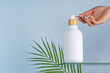 © ADDICTIVE STOCK - Hand presenting a bottle mockup with natural backdrop