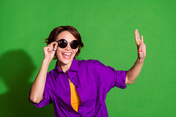 Wall Mural - Photo portrait of young positive lady with bob hair wearing stylish sunglass dancing hipster raised arm up isolated on green color background