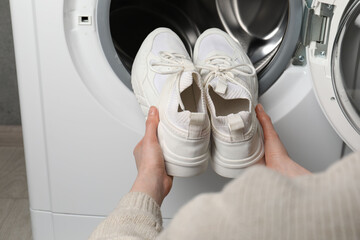 Poster - Woman putting stylish sneakers into washing machine, closeup