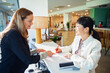 © Marko Geber - Two businesswomen at reception desk making a payment with smartphone at modern office