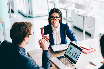 Two female colleagues have important meeting with male finance director of company discussing details of good trade indoors, group of economists sitting at desktop with laptop talking about statistics