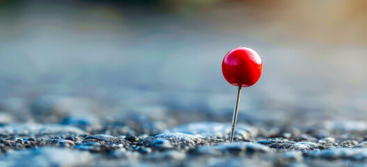 A red pin is stuck in the ground on a grey surface. The pin is the only object in the image, and it is the only thing that stands out. The image has a simple and minimalistic feel