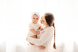 © Any Grant - mom and baby are playing and rejoicing in a bright white room on a white isolated window background, a mother with a small child hugs and kisses, happy motherhood with maternity leave, lifestyle