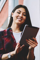 Wall Mural - Cheerful asian hipster girl enjoying leisure outdoors with modern portable pc while receiving positive email from friend, joyful woman watching funny videos on websites connected to 4g internet