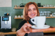 © Soloviova Liudmyla - Cheerfully smiling barista female giving white cup aromatic espresso at the coffee shop counter. Happy people, coffee consumption, beverages industry and small business concept image.