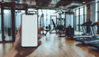 © *Lara* - A smartphone with white screen in the hand with fitness room in the background