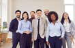 © Studio Romantic - Group of business multiethnic people men and women looking cheerful at camera and smiling indoors. Company employees or group of staff standing in office confidently. Team work concept.