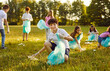 © Studio Romantic - Save planet. Portrait of little boy who collects trash in garbage bag in forest or in park. Smiling preteen boy collects trash on green lawn in background of his peers who pick up used plastic.