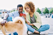 © BullRun - Pensive african american two bloggers dressed in casual wear spending leisure time together with dog in urban setting and watching video online on smartphone using free 4G internet connection