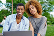 © BullRun - Portrait of happy couple in love with modern laptop device smiling at camera resting in urban setting.Positive african american young man with dark skinned girlfriend spending leisure time together