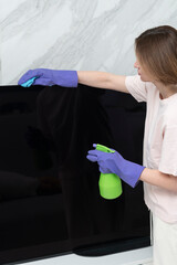 Close-up photo of young woman wiping television with a rag and spray	