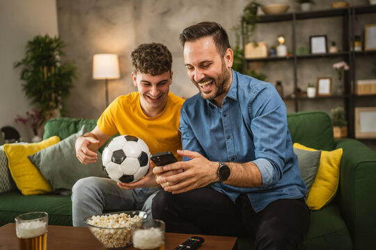 Two male friends follow football match results on mobile phone at home