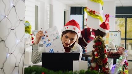 Wall Mural - Employee in Christmas decorated office happy to show management positive company profit during videocall. Worker in teleconference meeting talking with managers during xmas holiday season