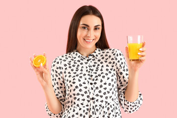 Wall Mural - Young woman with glass of juice and orange on pink background