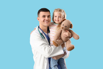 Canvas Print - Male pediatrician and little girl with teddy bear on blue background