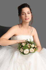 Wall Mural - Beautiful young bride in wedding dress with bouquet sitting on dark background