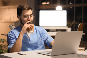 Sticker - Male nurse with coffee and laptop working evening shift at table in clinic