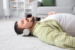 © Pixel-Shot - Young man in headphones lying on soft carpet at home, closeup