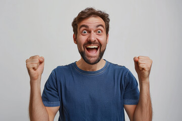 Wall Mural - Photo of an excited man wearing a casual t-shirt while raising fists up on a white background