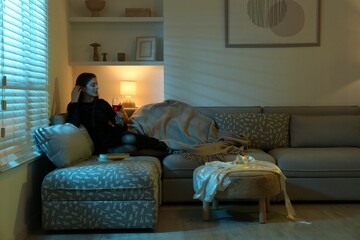 Canvas Print - Woman with glass of wine resting on couch in room at night