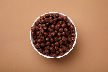 Chocolate cereal balls in bowl on brown table, top view