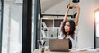 © Satori Studio - A woman is stretching her arms in front of a laptop on a desk. Concept of relaxation and focus, as the woman is taking a break from work to stretch and clear her mind